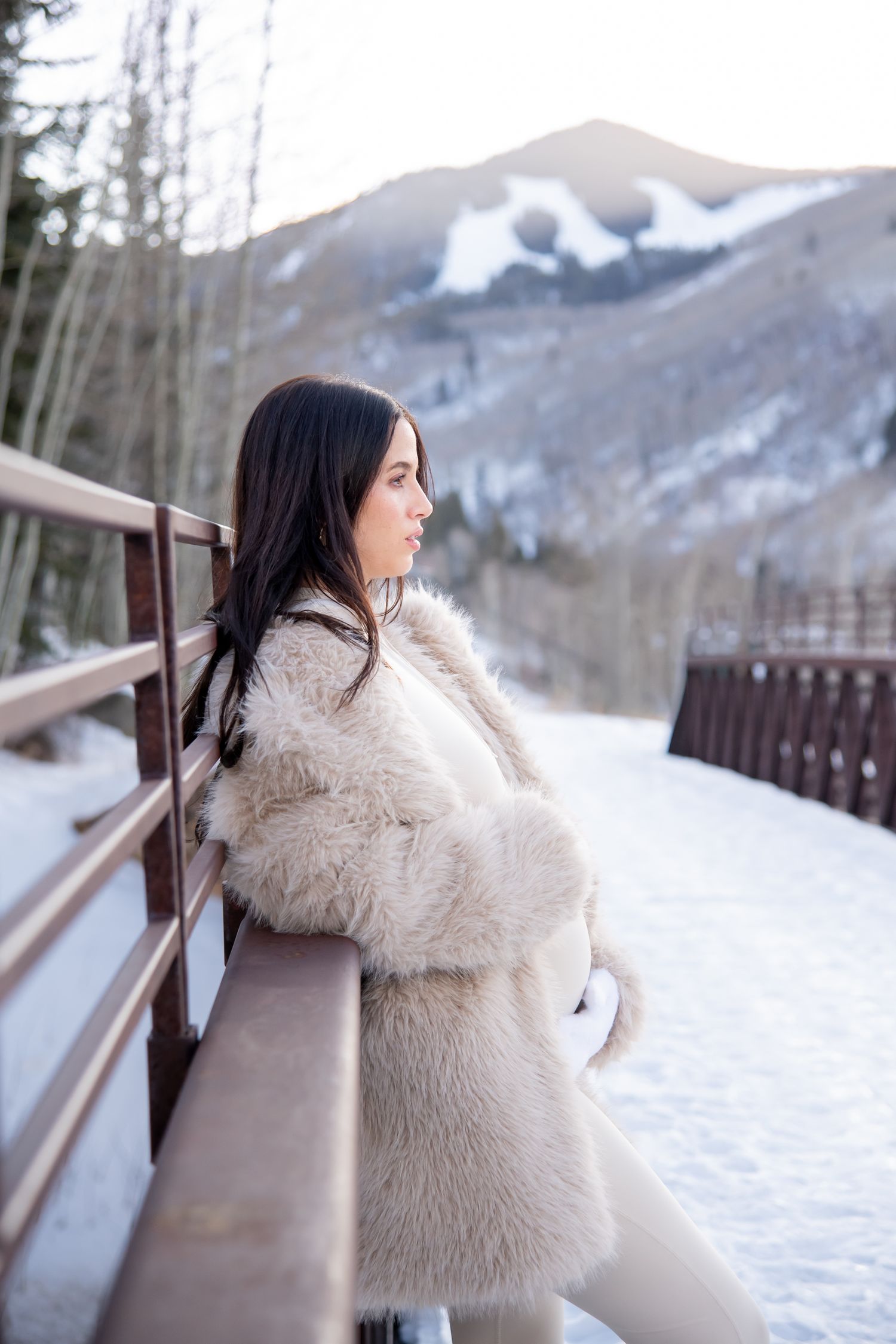 Stylish woman in fur coat stand for her maternity photo session in Vail Colorado