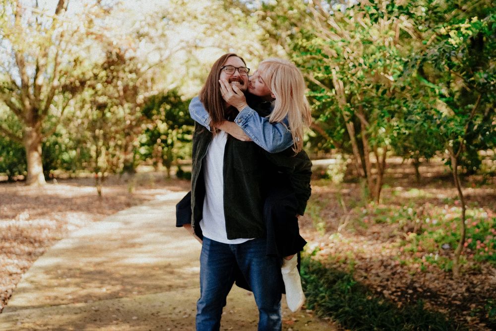 Two people share a joyful moment while embracing on an autumn path surrounded by trees.