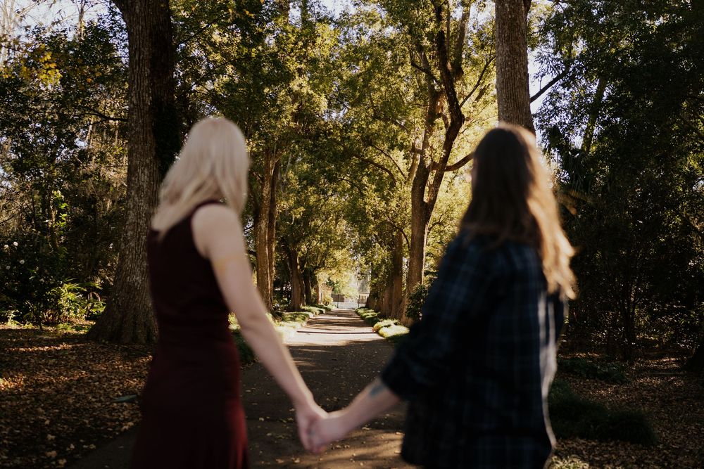A couple walks together through a sunlit wooded path during a romantic engagement photo session.