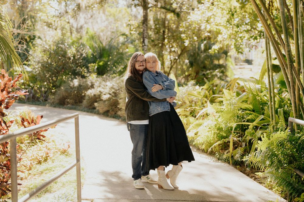 Two people share a tender moment while sitting on a wooden bench in a lush garden setting.
