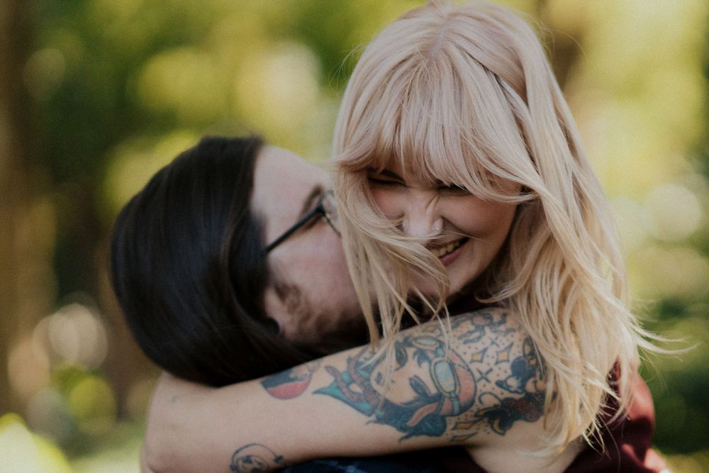 Romantic couple embraces in outdoor setting with natural sunlit background and soft bokeh effect.