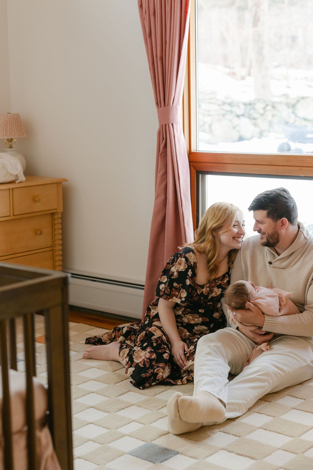 Couple sharing intimate moments while lying on a quilted mattress in a sunlit bedroom with wooden furniture.  In-home Newborn Session CT