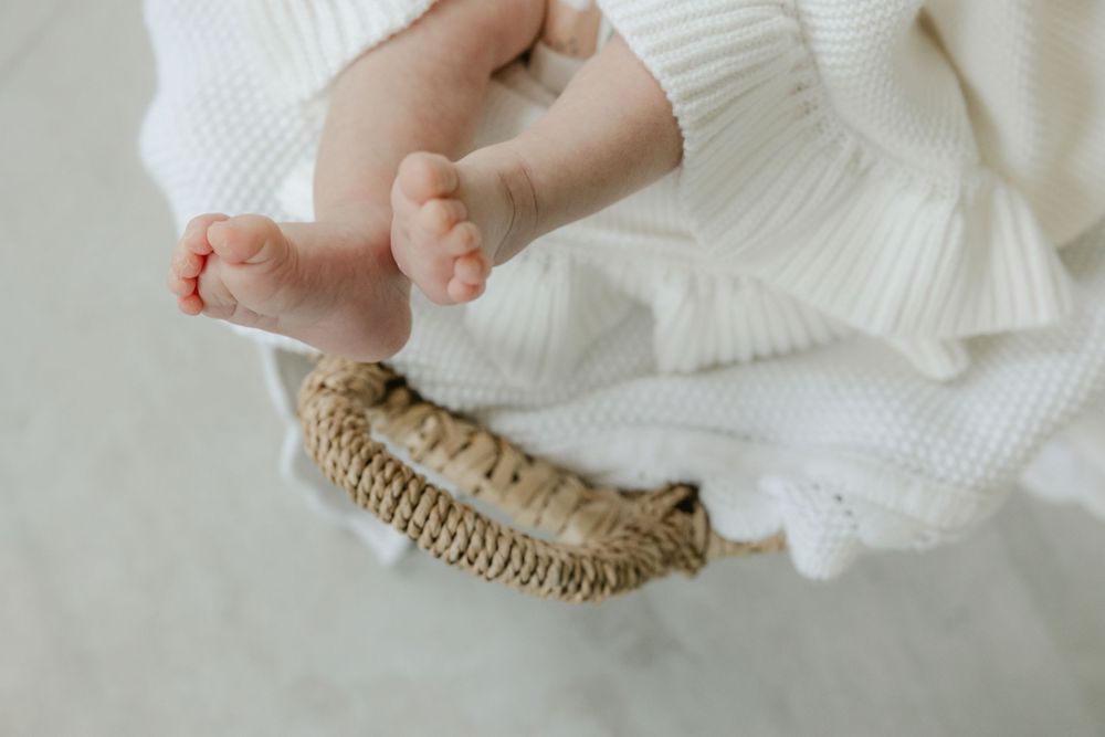 Tiny baby feet resting on a knitted beige blanket against white fabric background. Studio Newborn Photographer