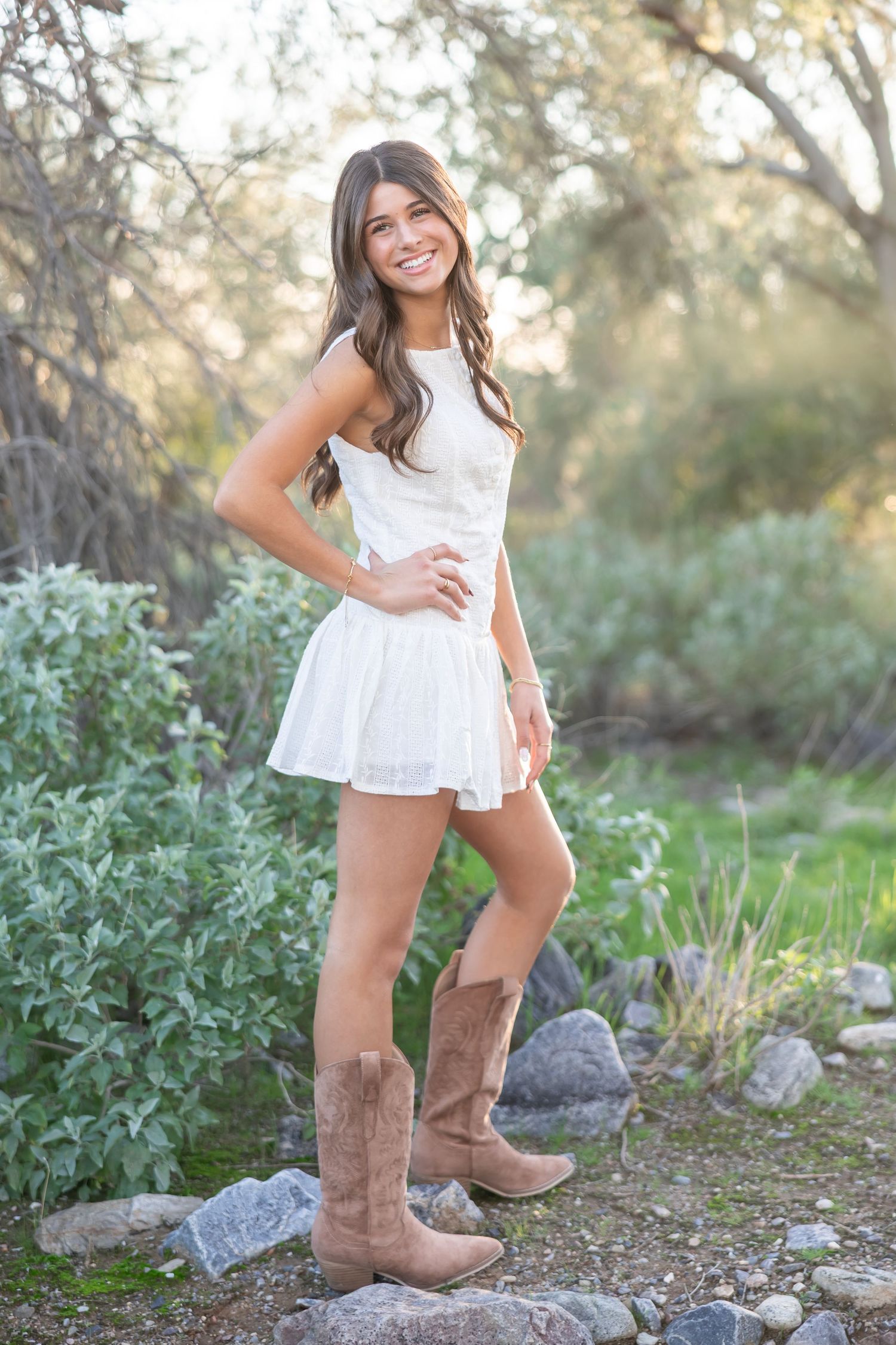 Brown suede cowboy boots paired with a white lace dress create a rustic countryside fashion look in an outdoor setting.