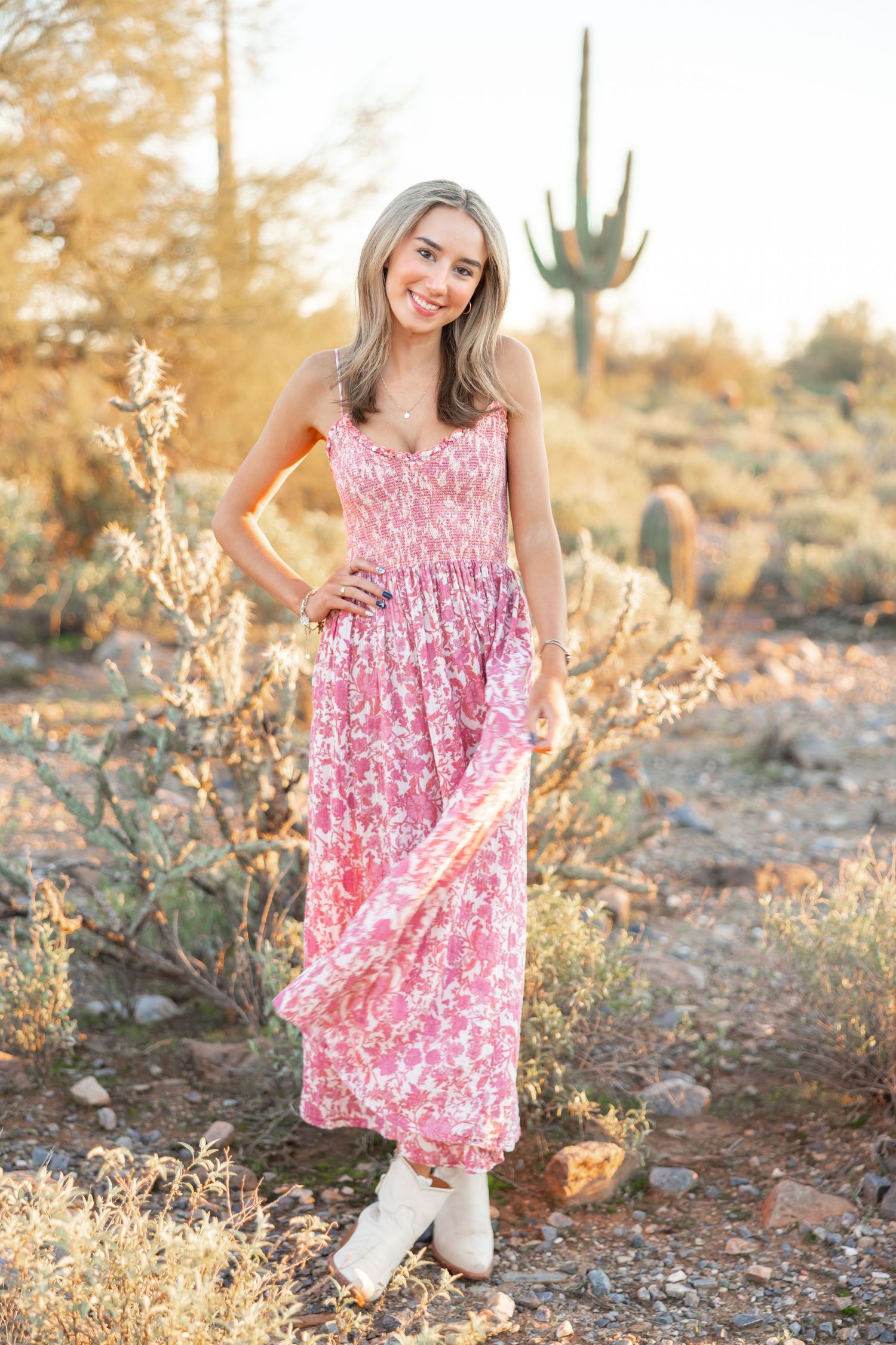 Pink floral maxi dress styled with white boots in a desert landscape with saguaro cactus at golden hour.