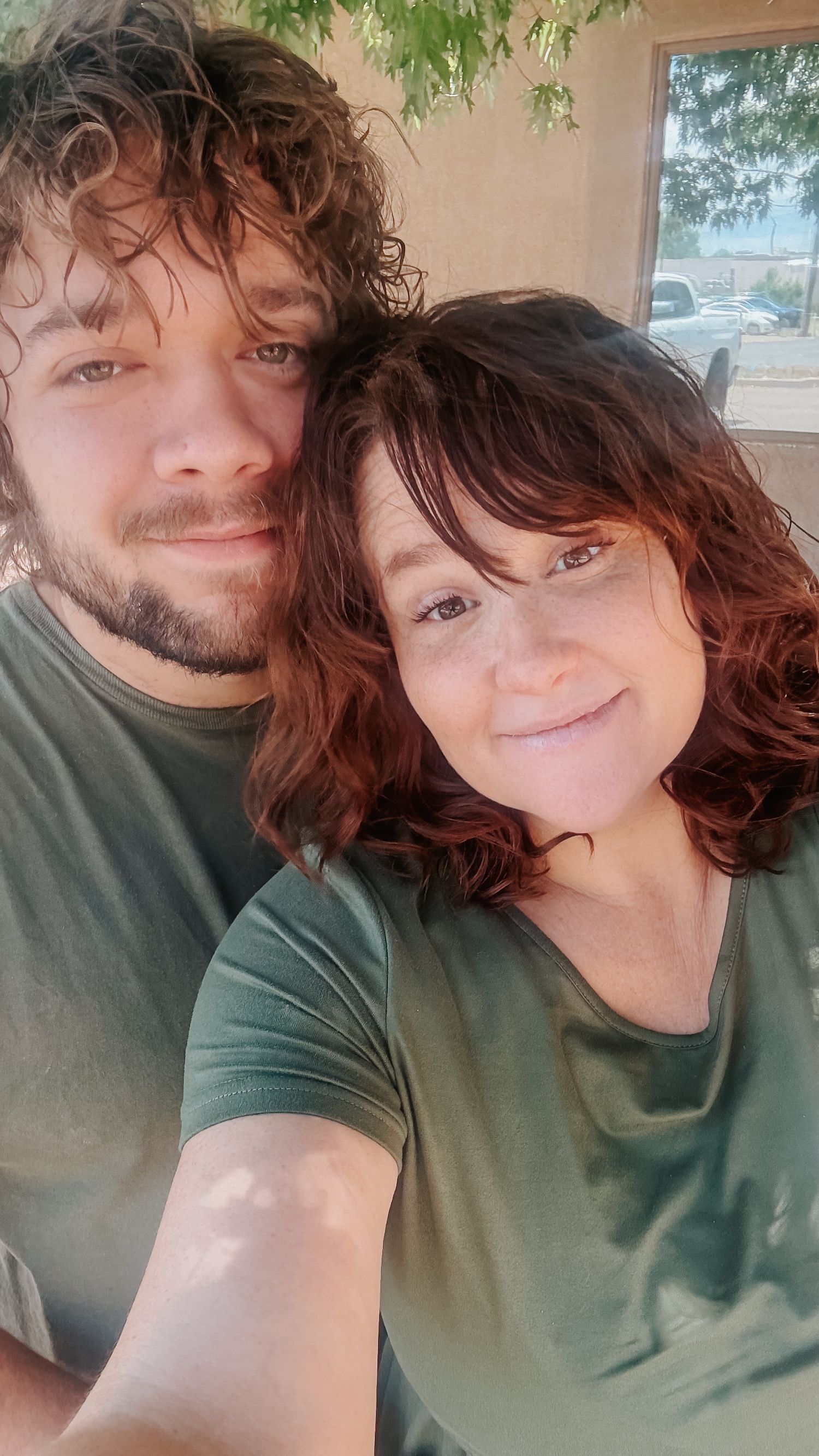 Selfie of couple wearing matching green shirts outdoors.
