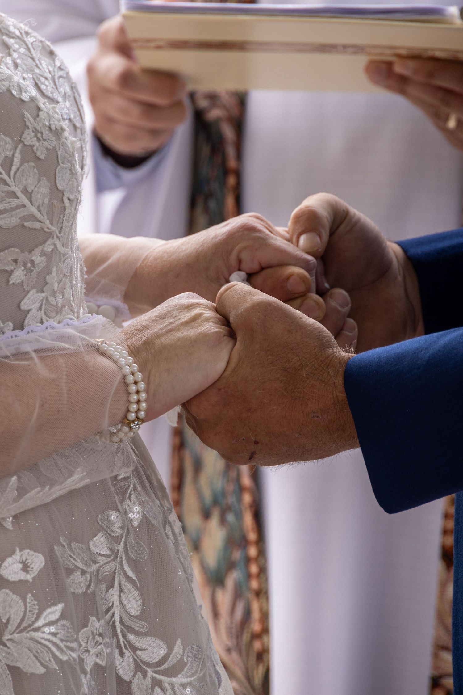 frederick maryland wedding  Close-up of hands exchanging wedding rings during a ceremony with lace dress and pearl bracelet details.
