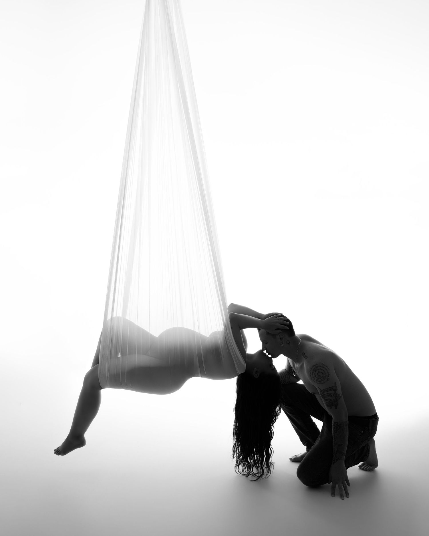 Artistic black and white silhouette of a person posing with aerial silk fabric in a dramatic backbend position.