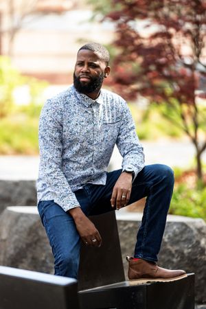 Casual outdoor portrait session featuring floral print shirt and denim against stone wall backdrop.