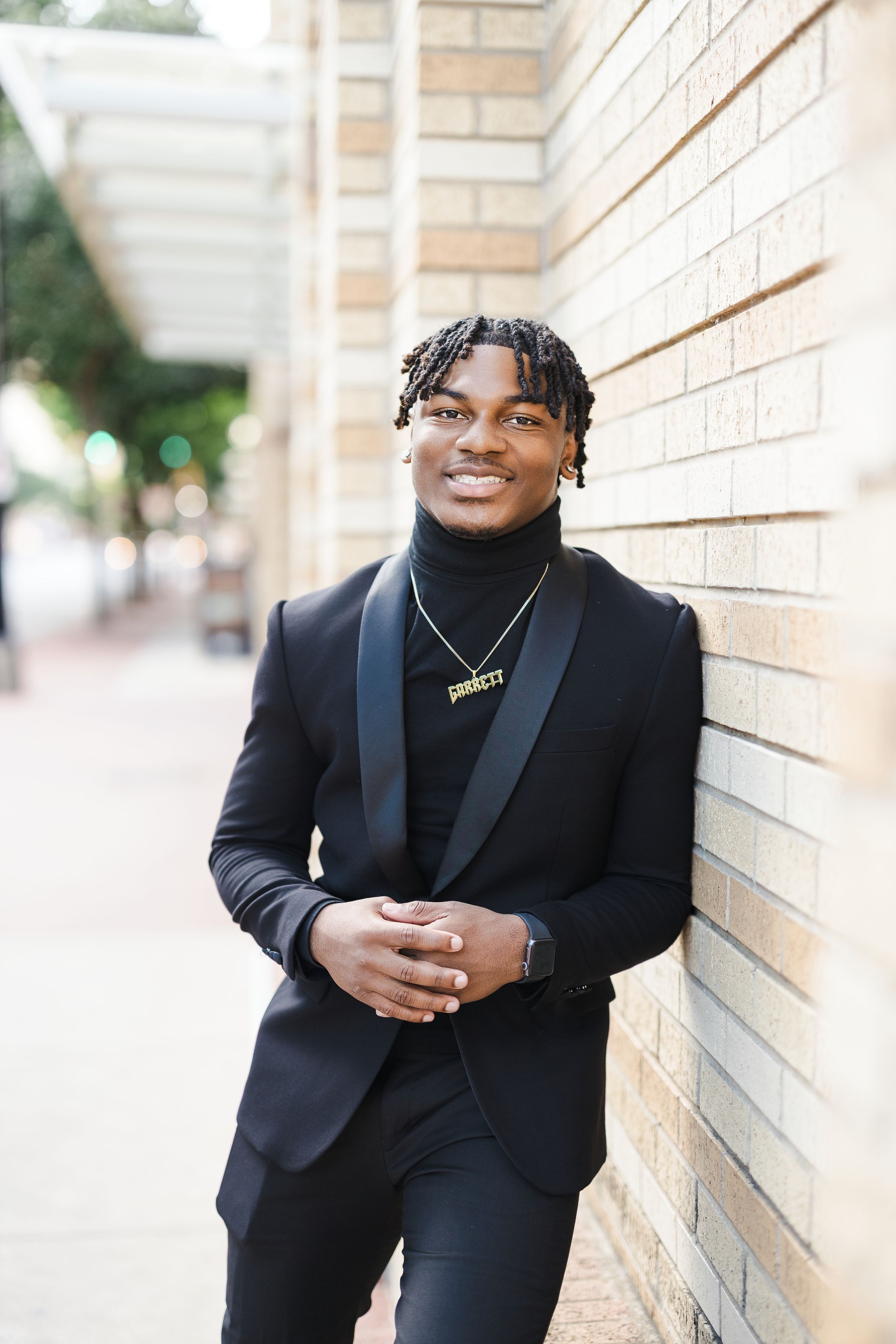 Person in black blazer posing against brick wall in outdoor portrait session.