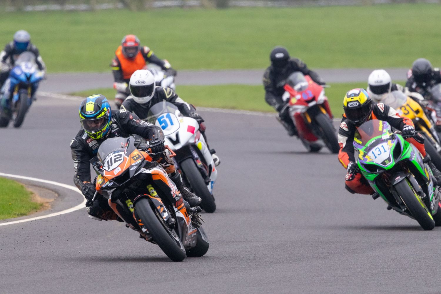 Motorcycles racing on a racetrack during a competitive motorsport event with riders leaning into turns at high speeds.