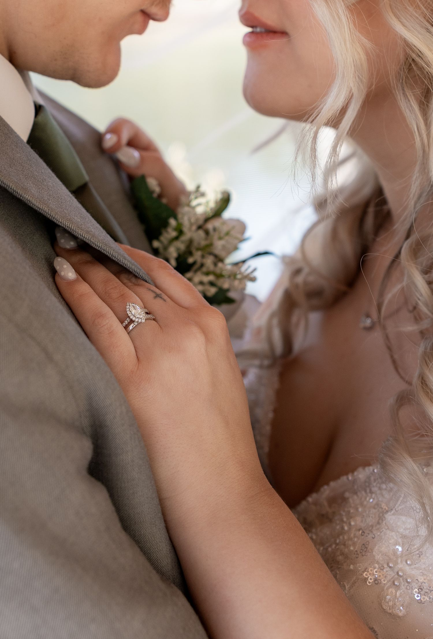 Close-up of bride and groom nearly kissing, showcasing a diamond halo engagement ring and wedding band on her hand.