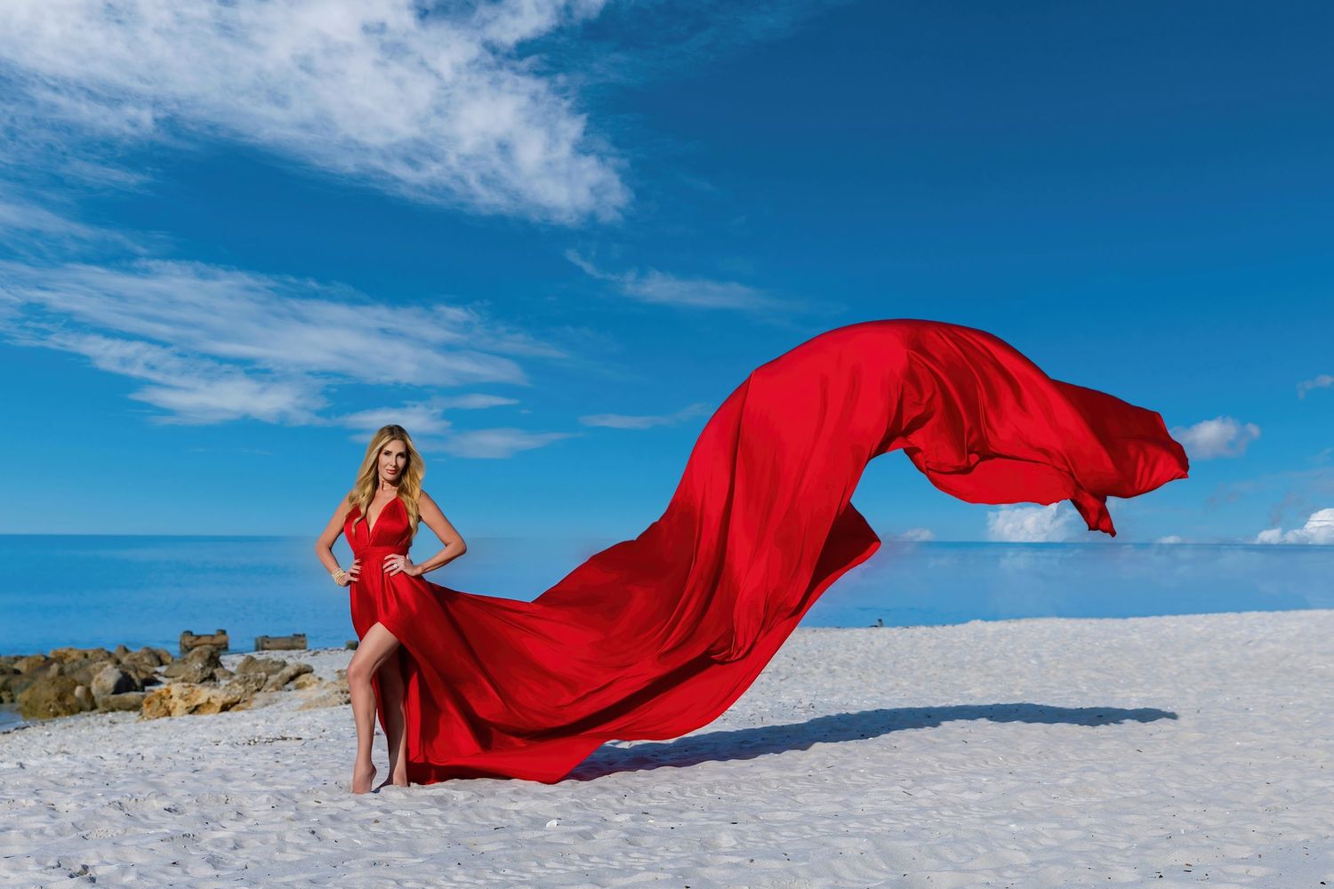 A flowing red dress billows dramatically against a stark white salt flat landscape under bright blue skies.