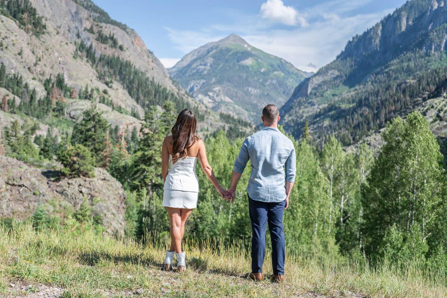 An eloping couple hold hands while looking out at a scenic mountain valley with evergreen trees and rugged peaks in Ouray.