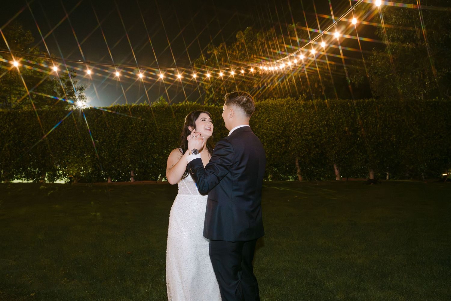 String lights create a romantic ambiance above a couple sharing a tender moment at an evening wedding.