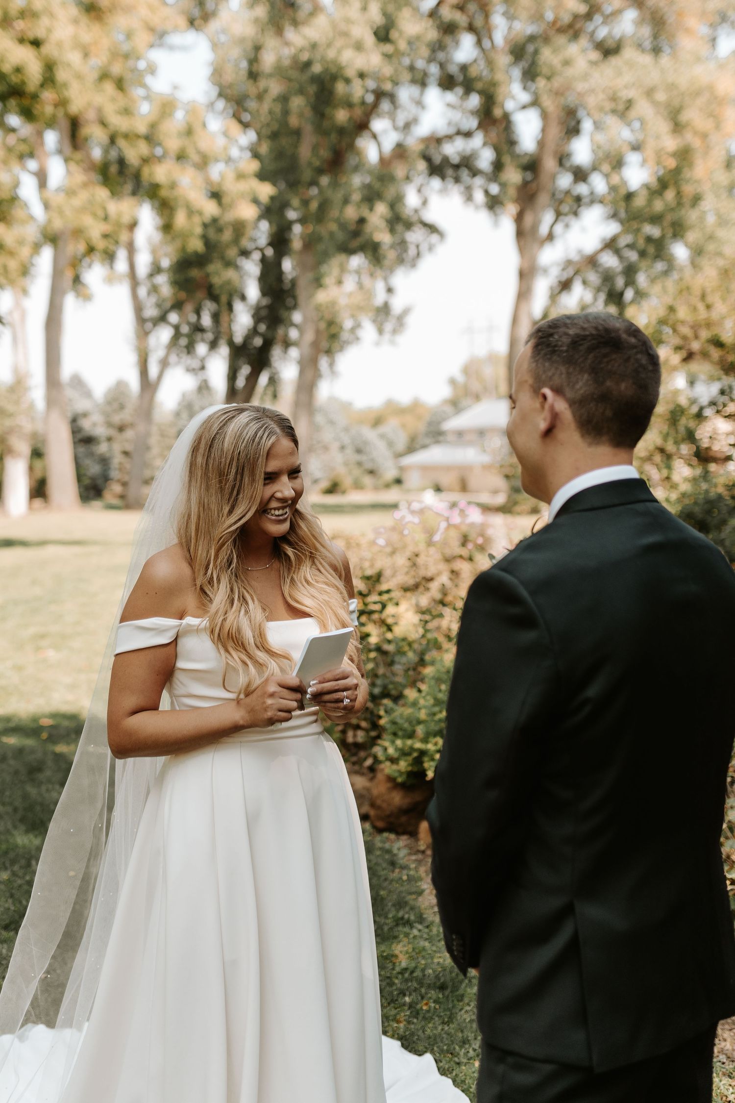 A bride reads her vows during an outdoor wedding ceremony surrounded by trees.
