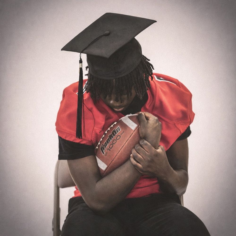 Graduate in red academic regalia holds diploma while posing.