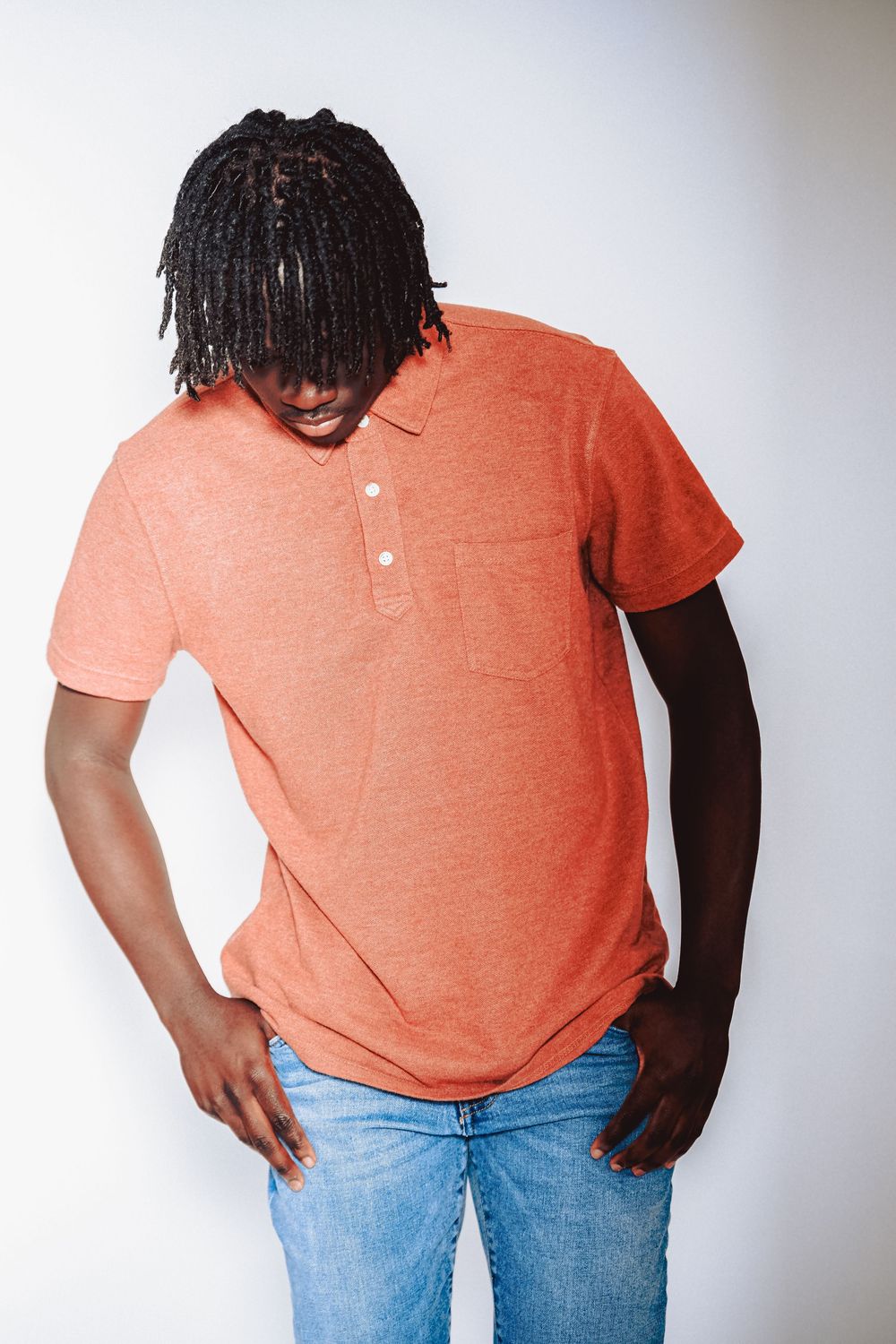 Person in coral polo shirt and jeans poses against white background.