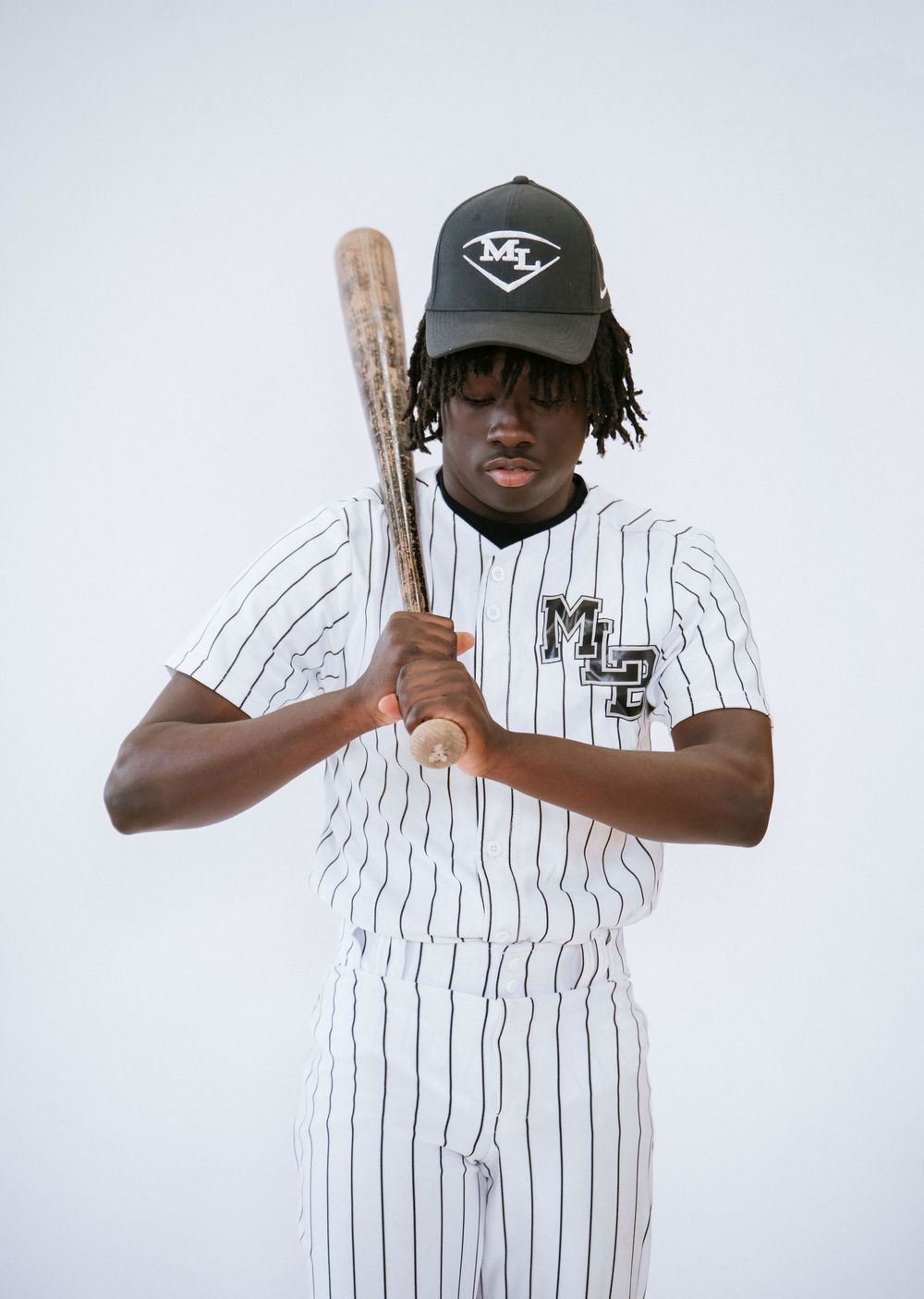Person in pinstriped baseball uniform demonstrates batting stance.