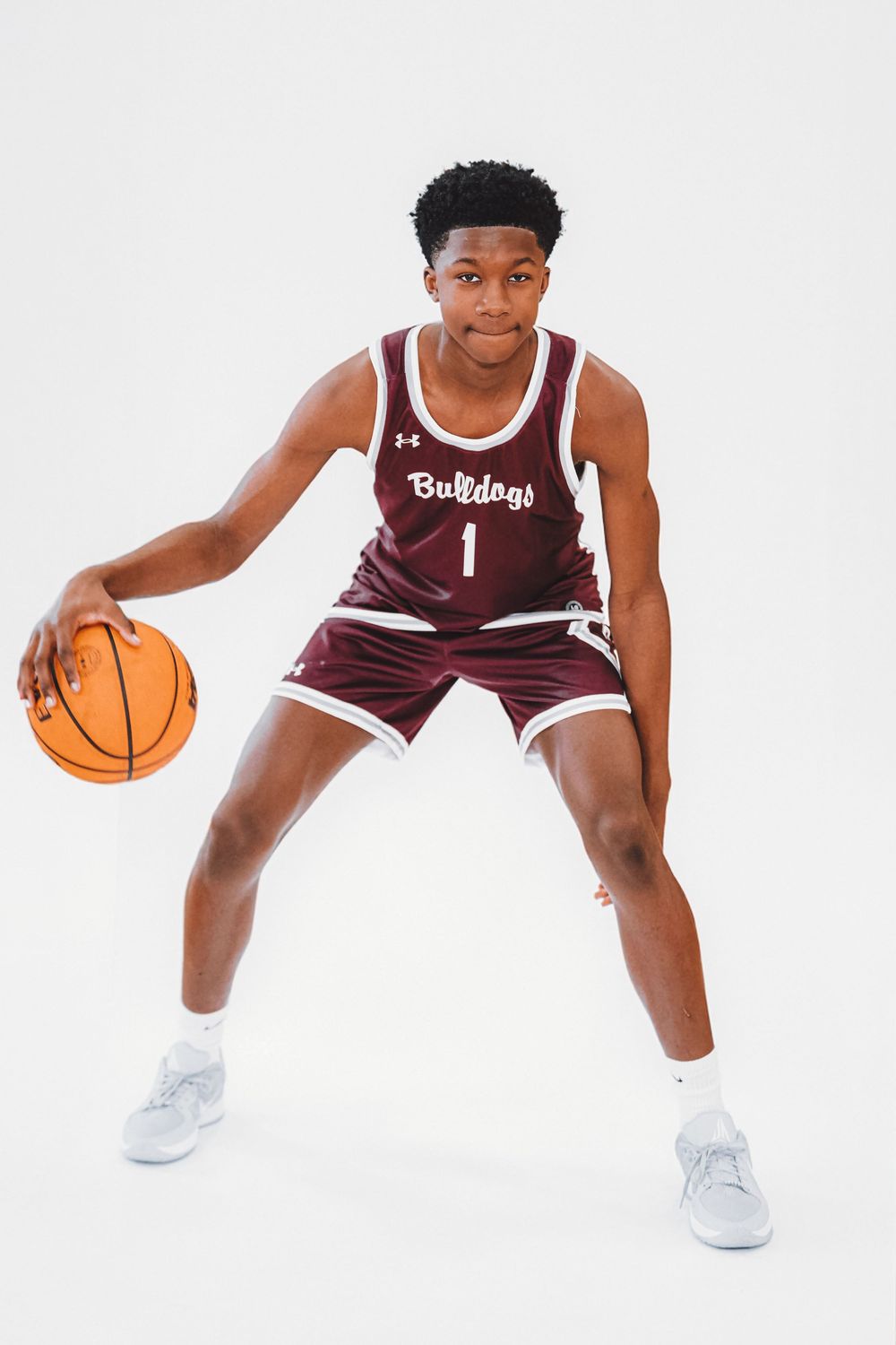 Basketball player in maroon Bulldogs uniform demonstrates dribbling stance with ball.