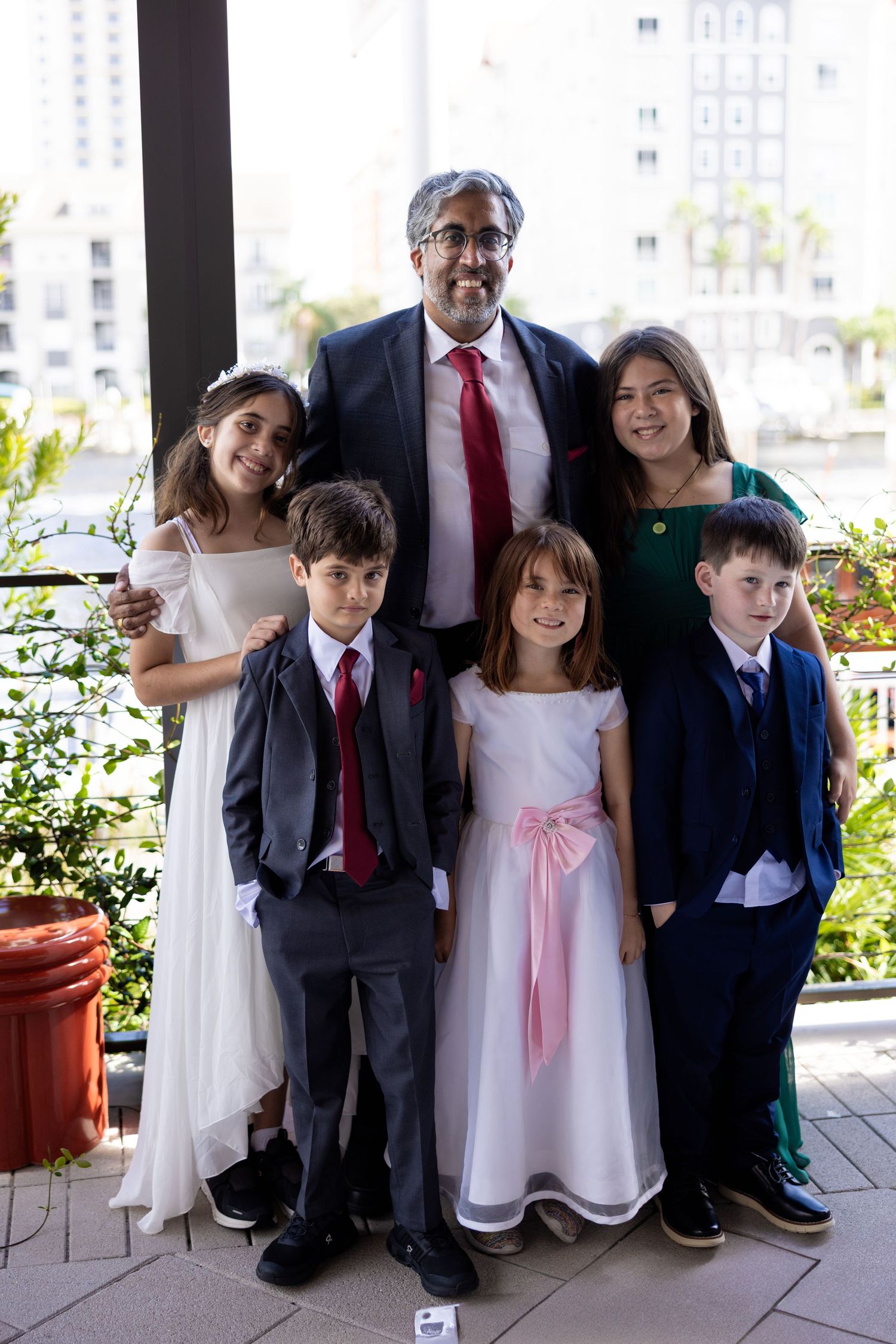A group of children and adults in formal attire pose together on a porch during a special occasion.