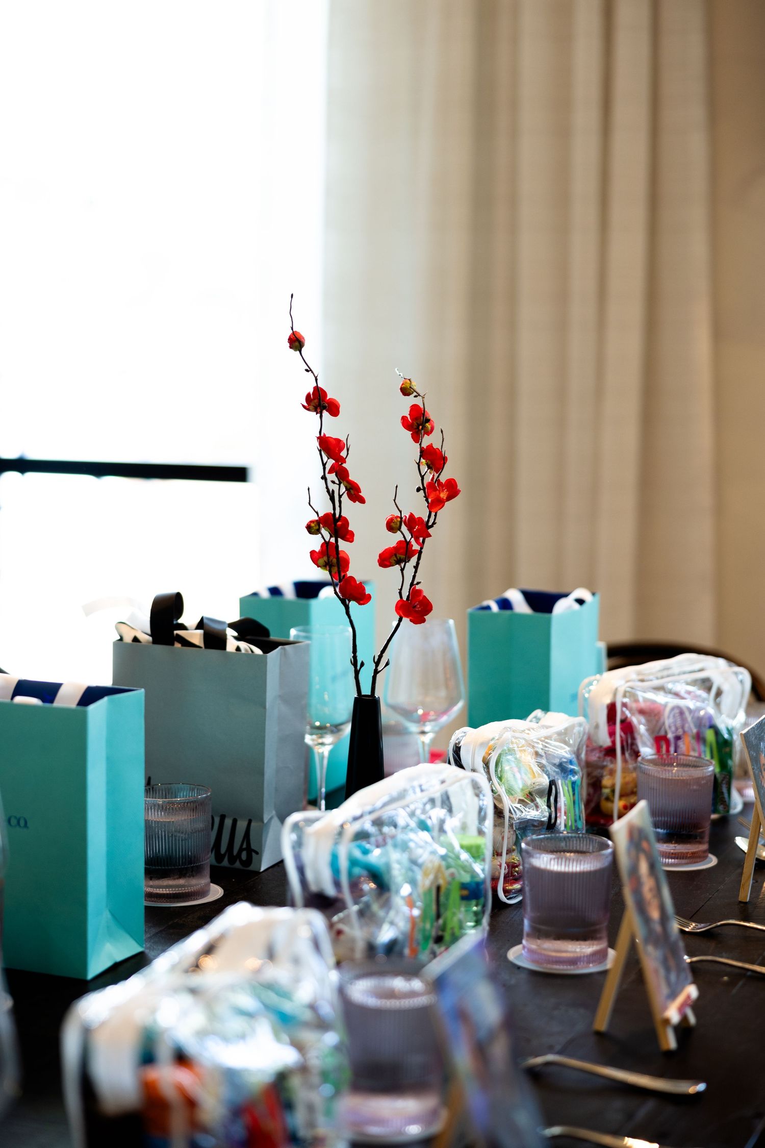 Elegant table setting with teal blue gift boxes and red floral accents on dark wood surface.