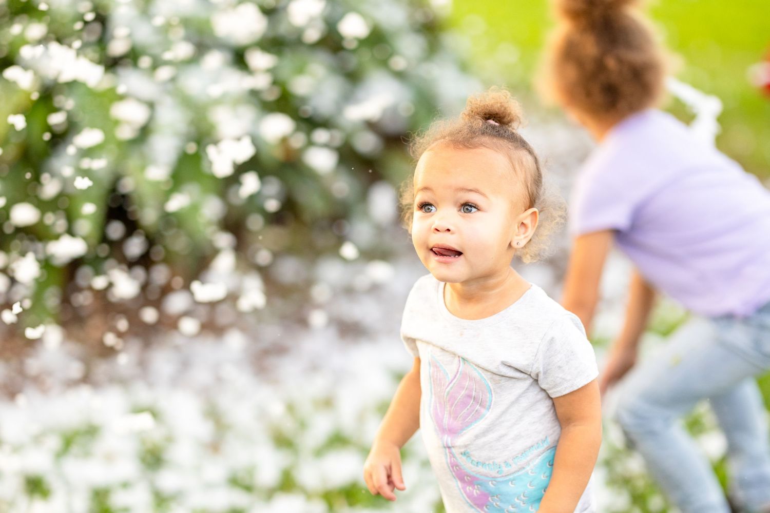 Blurred action shots of children playing outdoors with white flower petals falling in the sunlight.