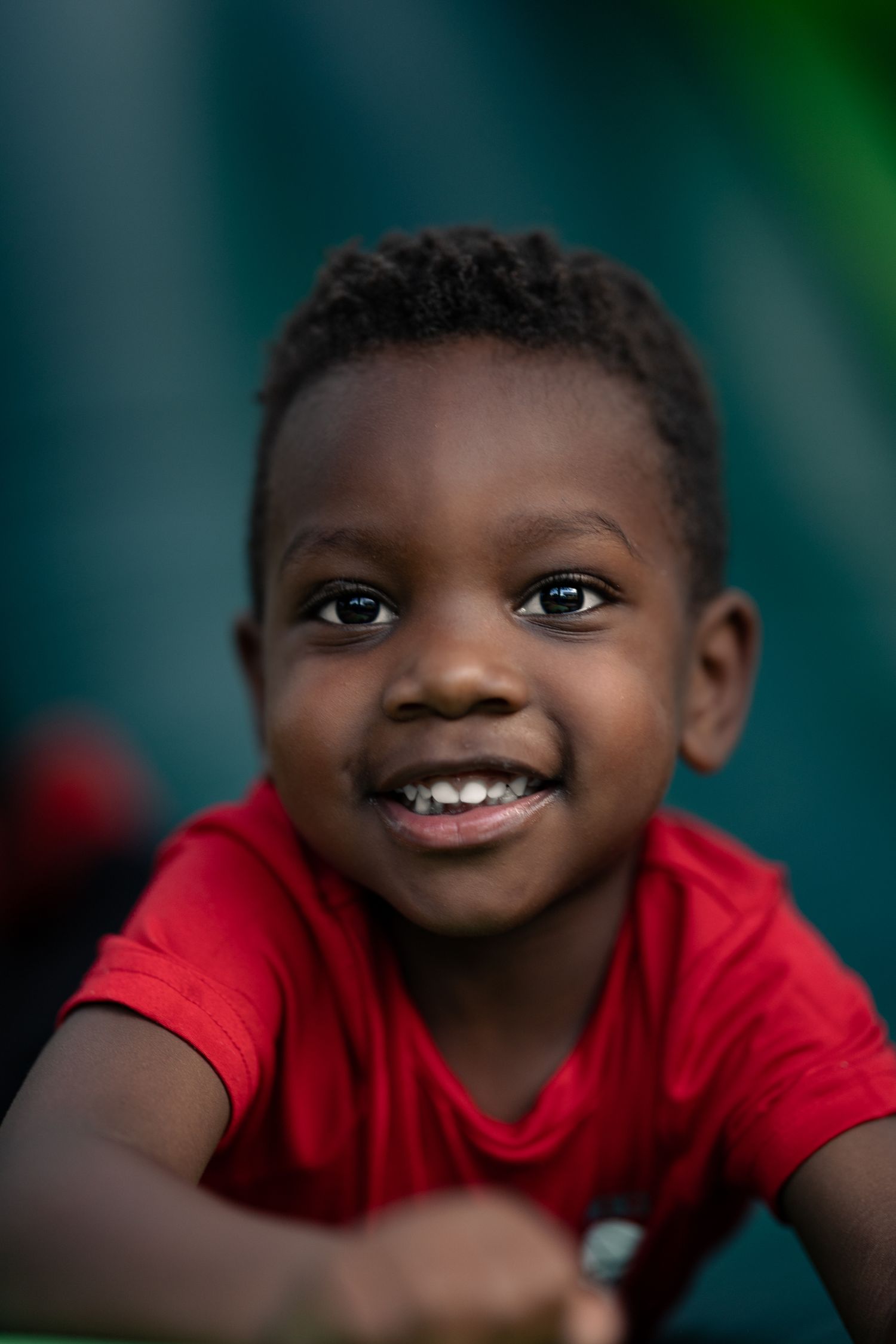 Close-up portraits of a young child in a red shirt showing joyful expressions against a blurred green background.