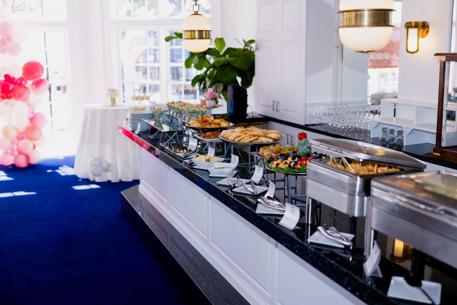 A white and navy blue catering buffet setup with chafing dishes and serving stations at an elegant event space.