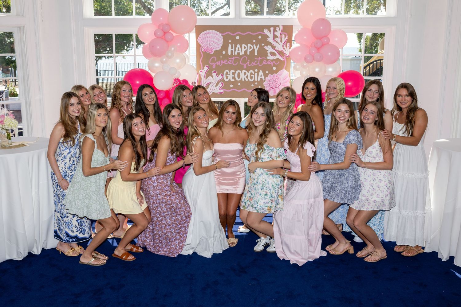 A group of people in floral and pastel dresses pose together at a celebration event.