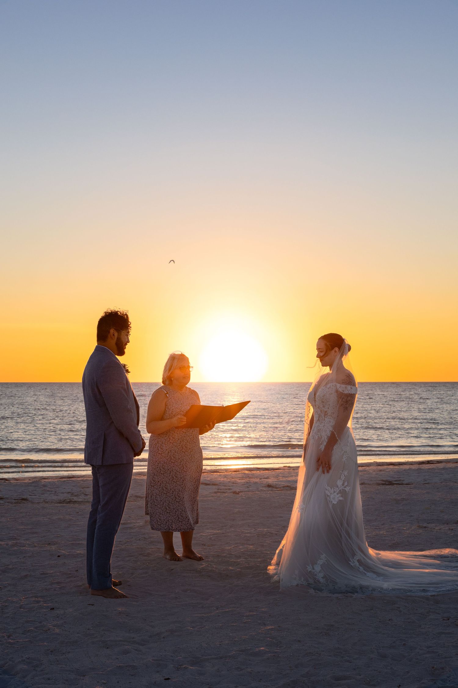 A wedding ceremony silhouetted against a vibrant orange sunset on a peaceful beach.