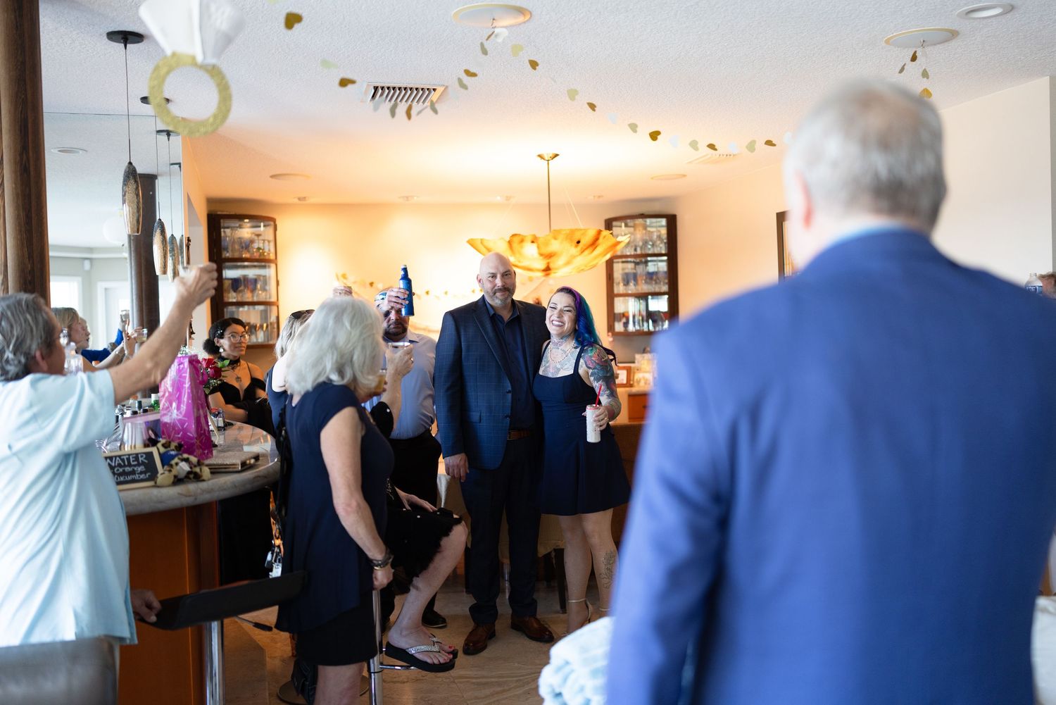 People gather in a bright indoor space for a social event with multiple conversation groups visible.