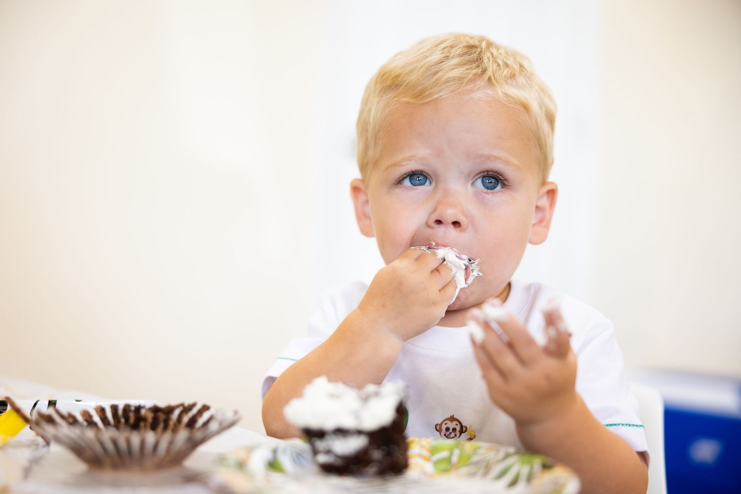 A child with blonde hair eats a cupcake while sitting at a table.