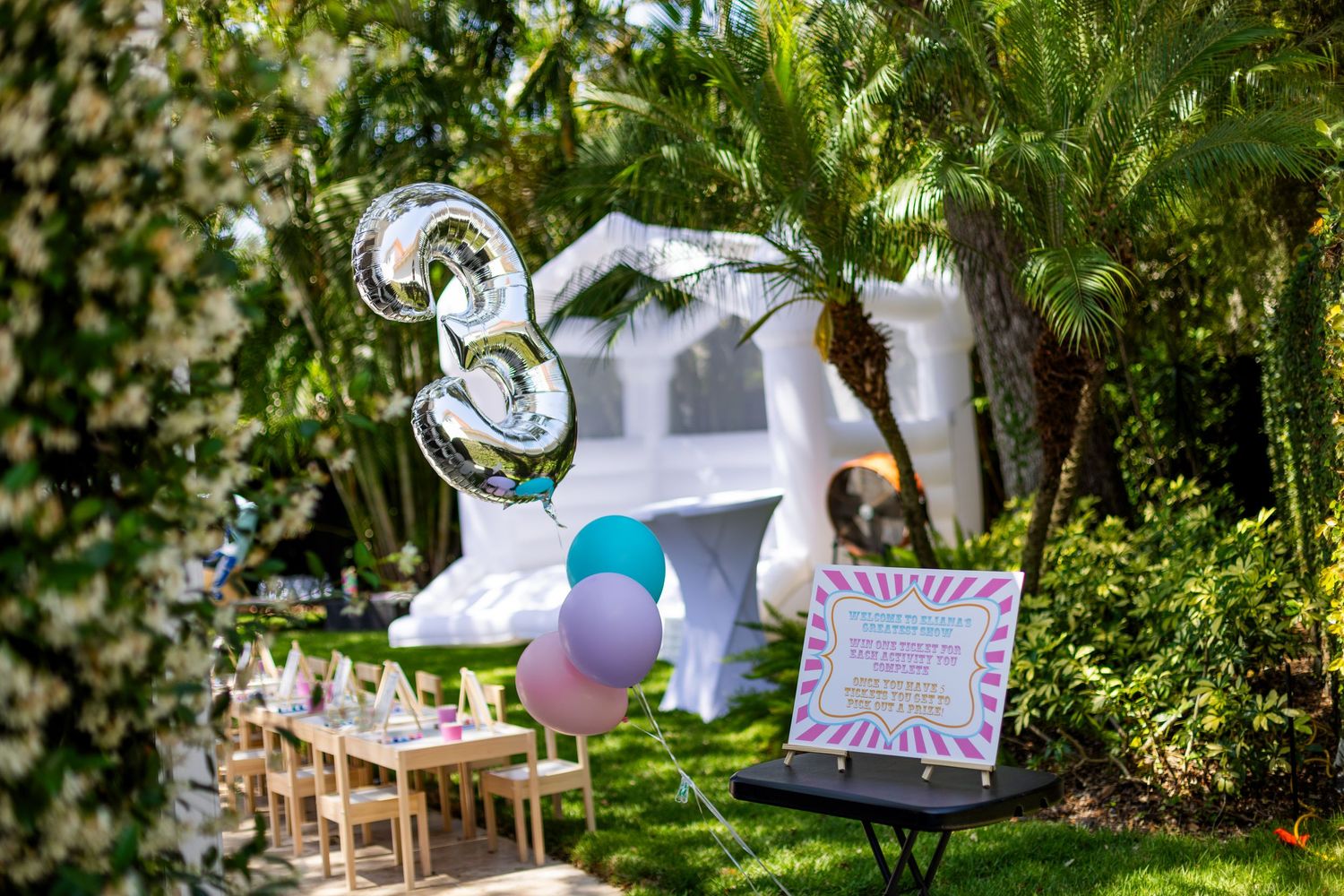 Colorful balloons and decorative sign displayed at an outdoor garden party setup with natural greenery backdrop.