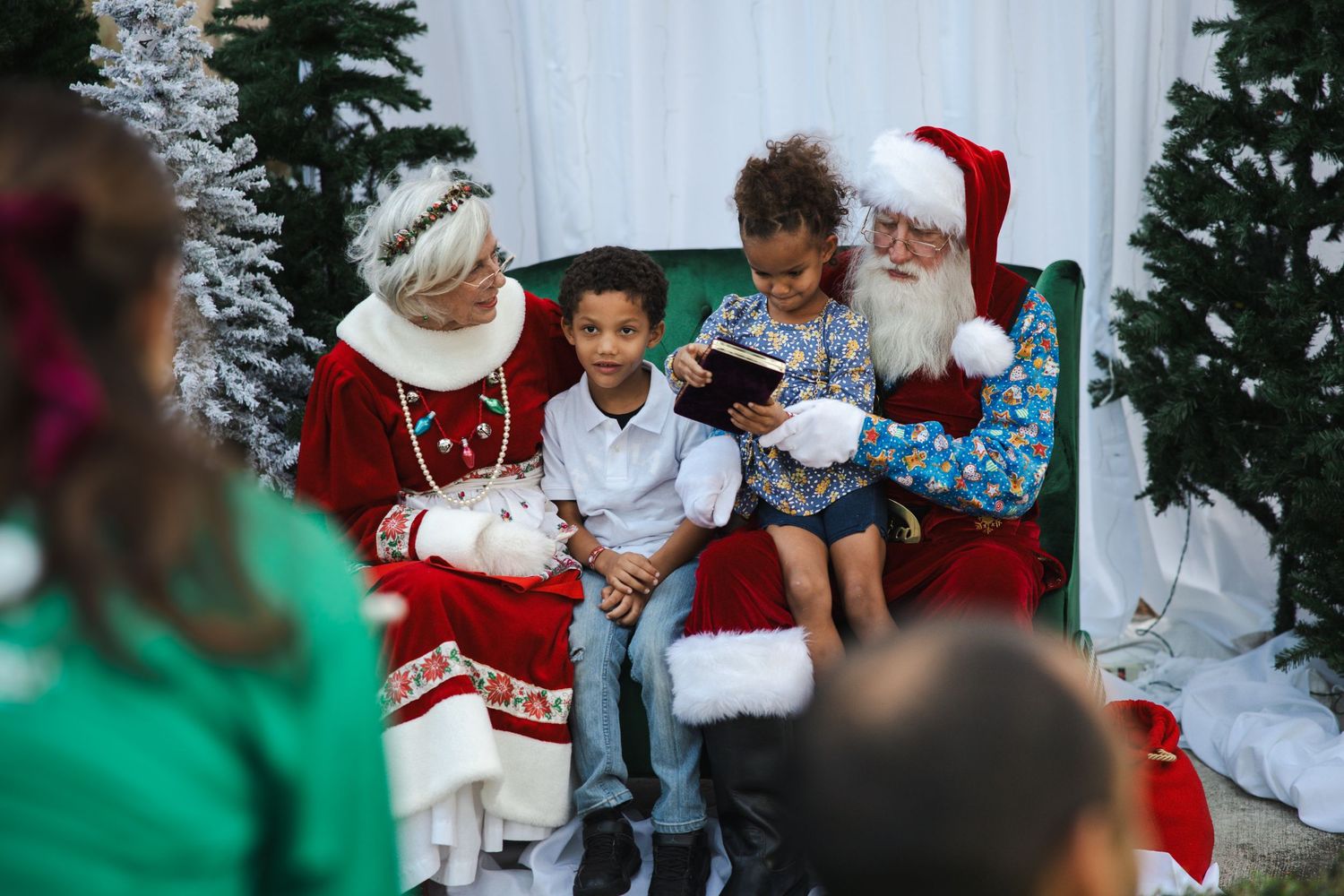 A holiday scene with festive decorations and visitors meeting Santa and Mrs Claus.