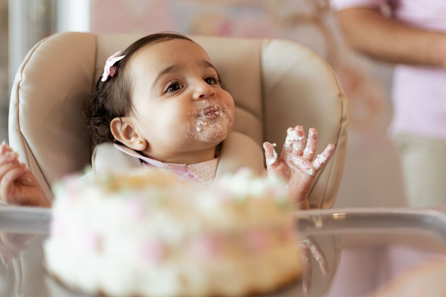 A small child celebrates with cake and frosting on their face during a birthday party.