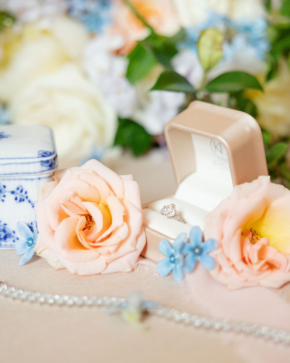 Delicate peach roses and blue flowers surround an engagement ring box in an elegant table setting in St. Paul, Minnesota.