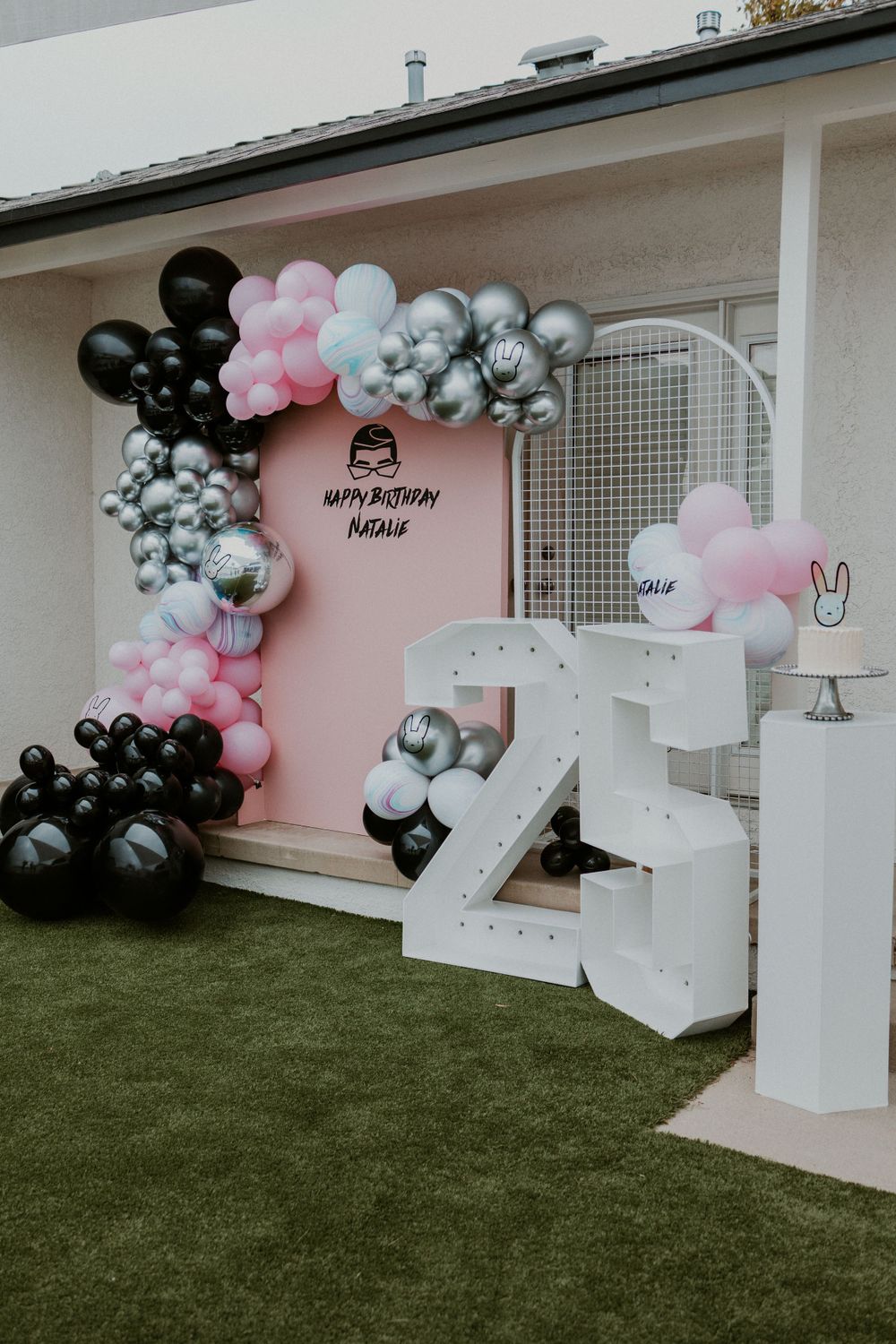 Modern party setup with pink backdrop, balloon garland, and large white number 25 display.