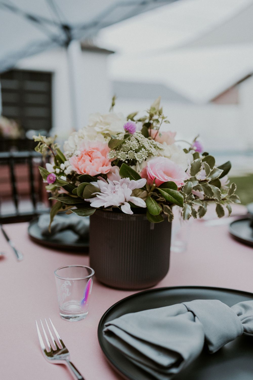 Elegant table setting with pink roses in dark vase on pink tablecloth with black plate and napkin.