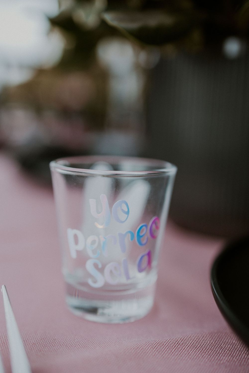 Close-up of clear shot glass with 'Partners Soda' text on pink tablecloth.