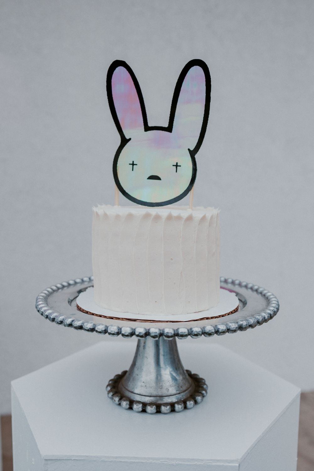 White buttercream cake with cute bunny topper on a silver pedestal cake stand.