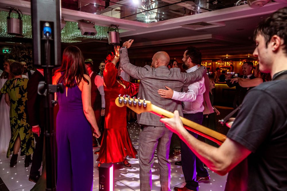 Lively wedding reception dance floor with live band guitarist performing for celebrating guests.