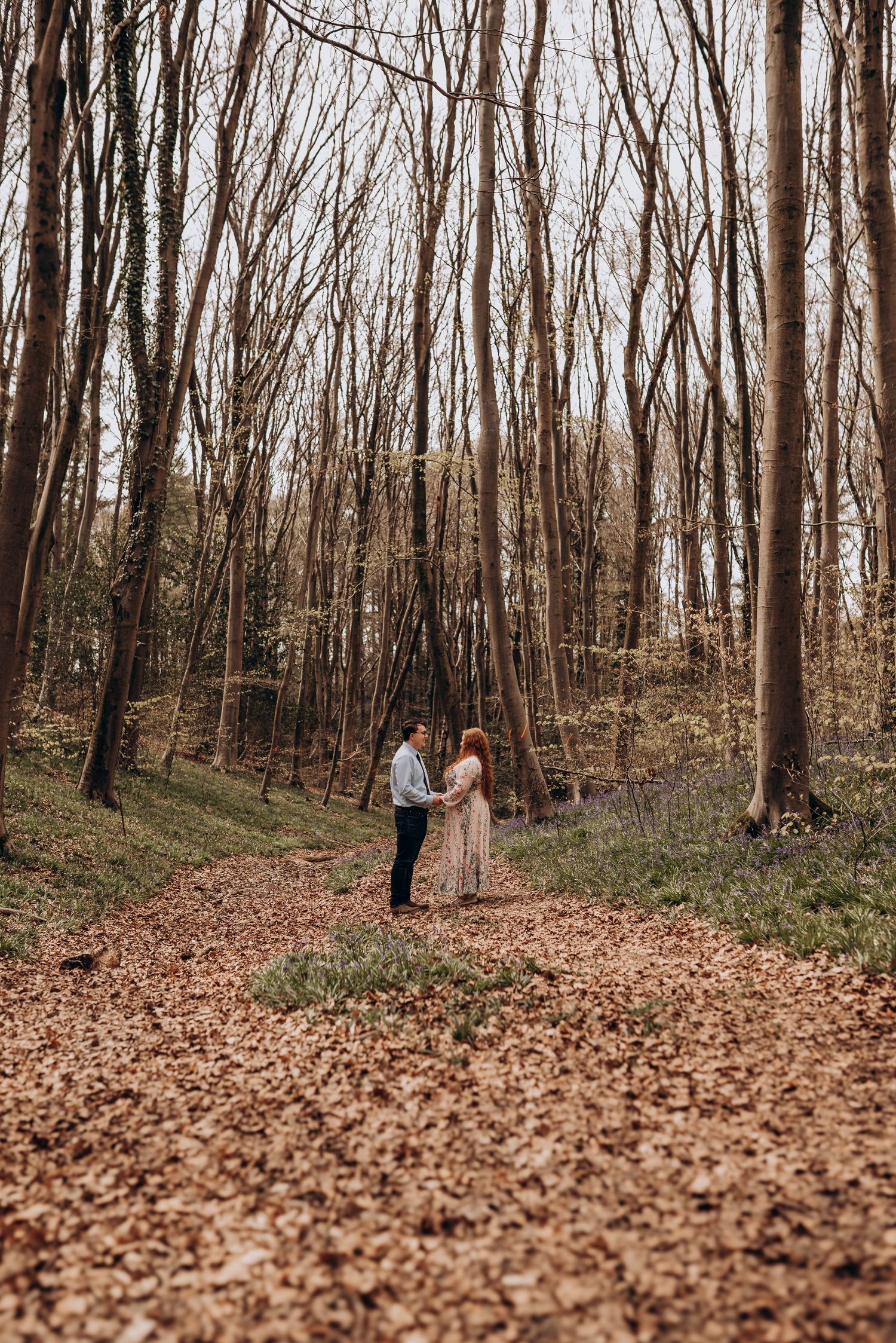 Wide panoramic view of a wooded forest path covered in fallen autumn leaves.
