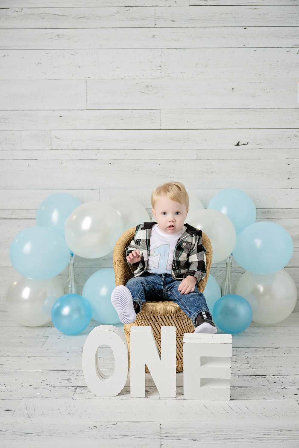 Birthday setup featuring rattan chair, blue and white balloons, and ONE letters on wood background.