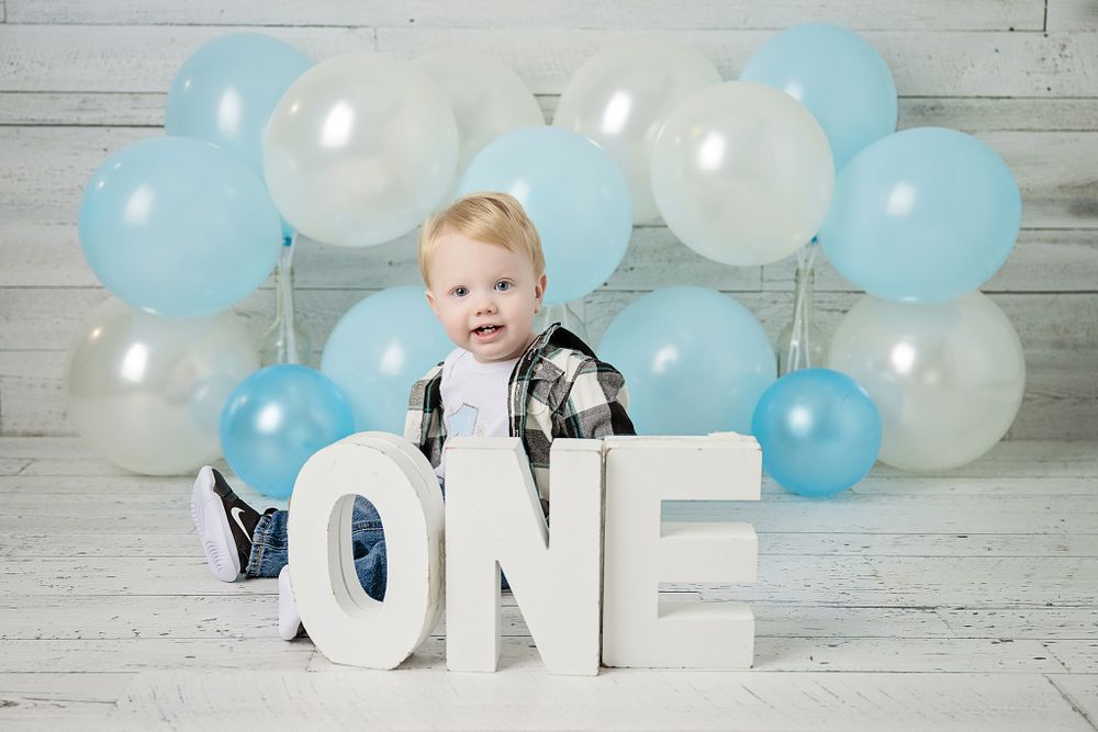 Birthday photo setup with blue and white balloons and ONE letters on white wood backdrop.