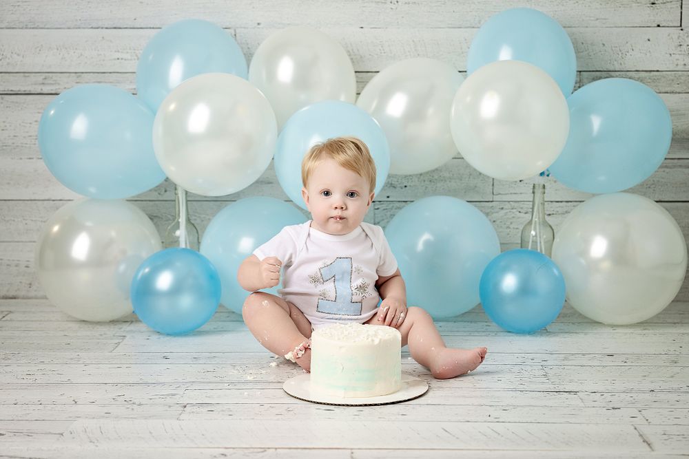 First birthday celebration setup with white cake and blue and white balloon decorations.