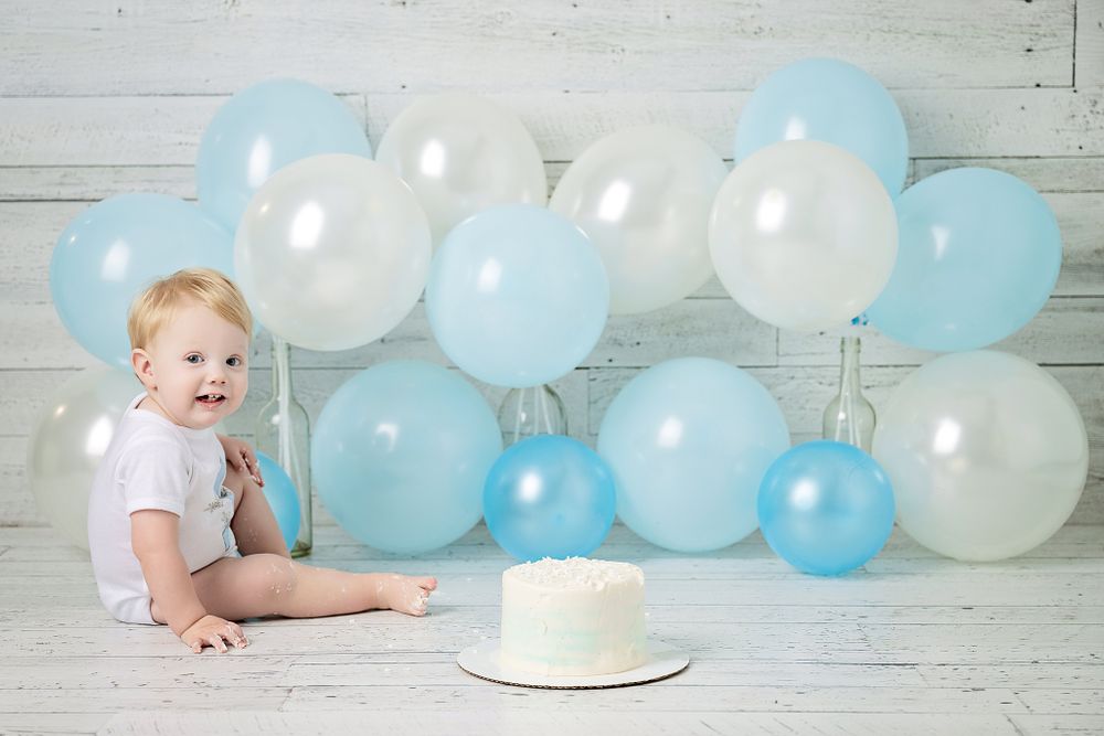 Birthday photo session with white cake and blue and white balloon arrangement.
