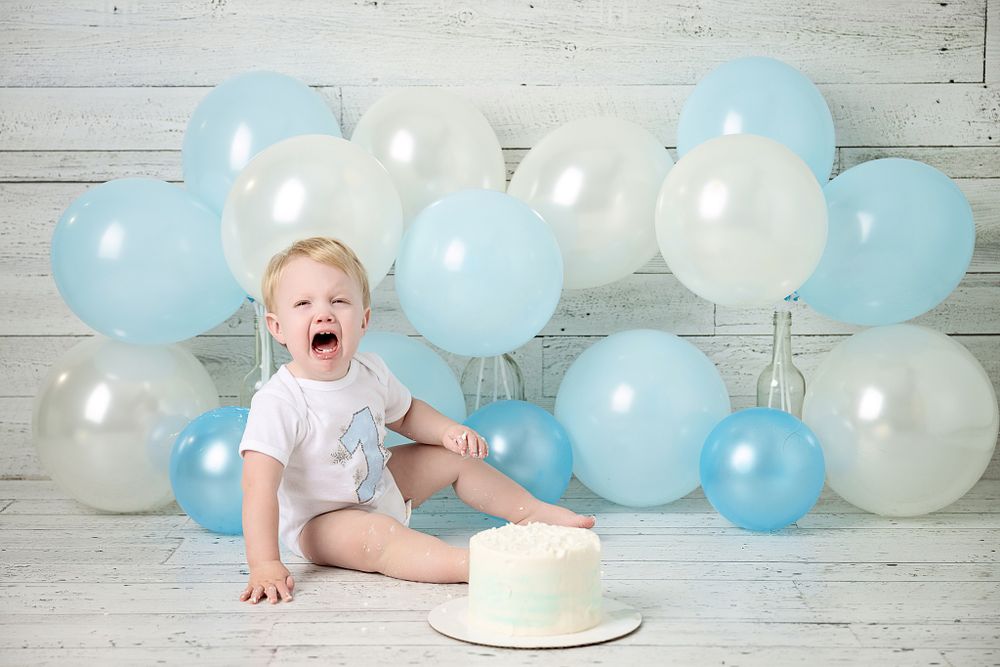 First birthday celebration with white cake and festive blue balloon background.