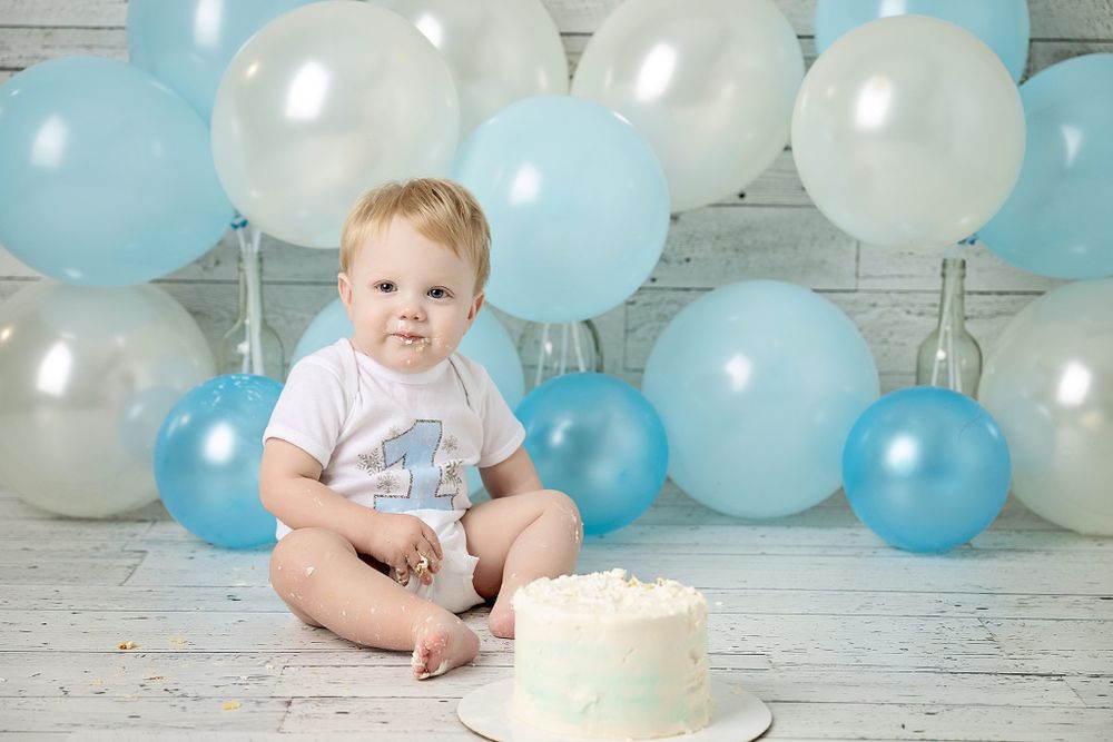 First birthday photo with white smash cake and blue and white balloon display.