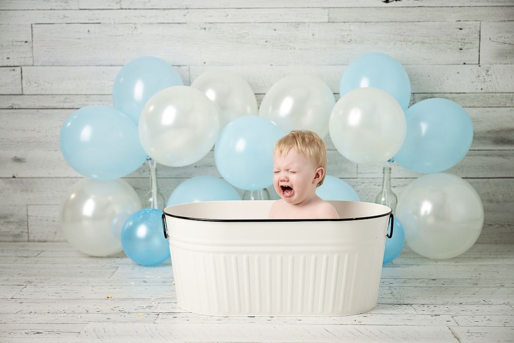Baby bath photo shoot with white tub and blue and white balloon background.